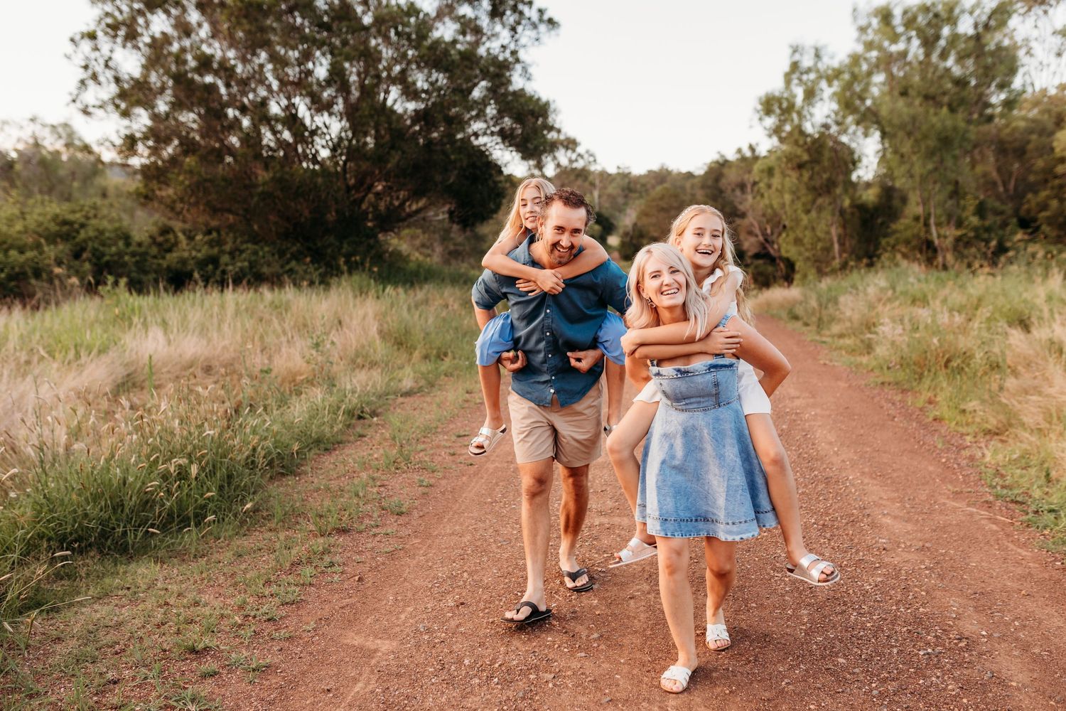 Family walking and playing together on rustic dirt path during sunset.