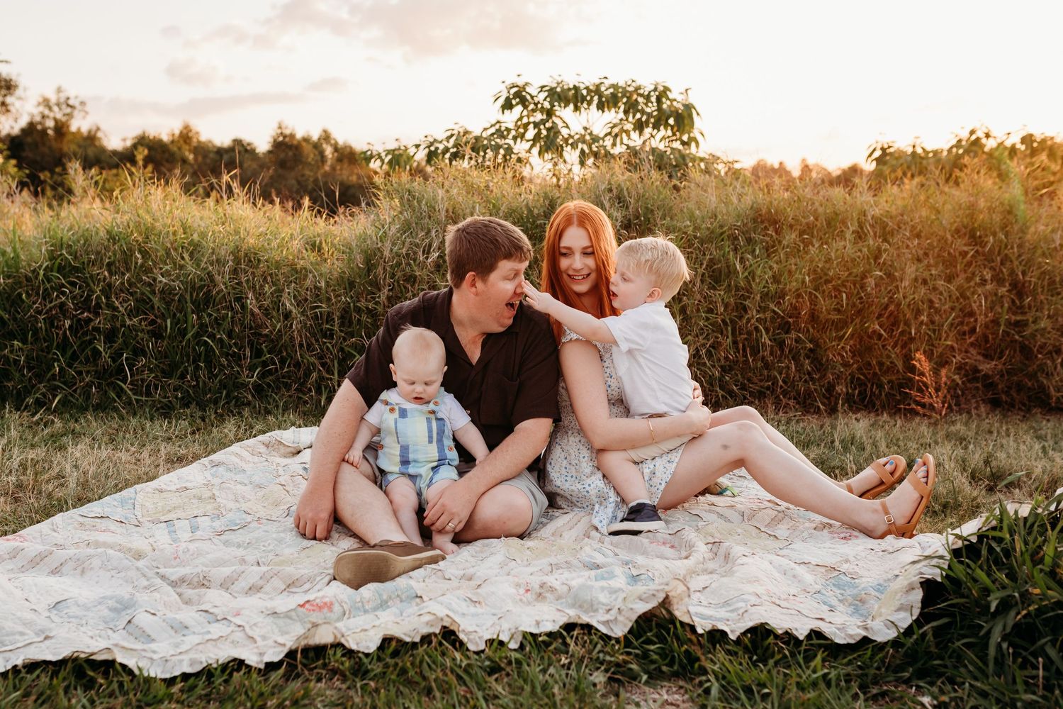 Family relaxing on white blanket in field during golden hour photo session.