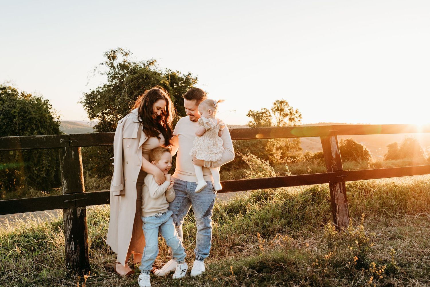 Family leaning on wooden fence during sunset photoshoot in countryside setting.