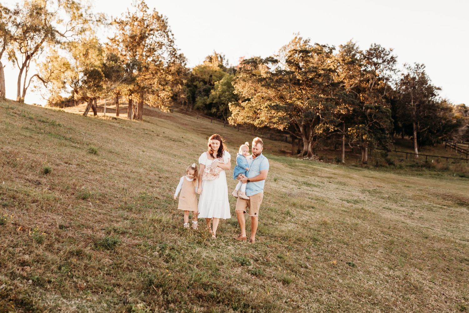 Family walking together on a grassy hillside during golden sunset.