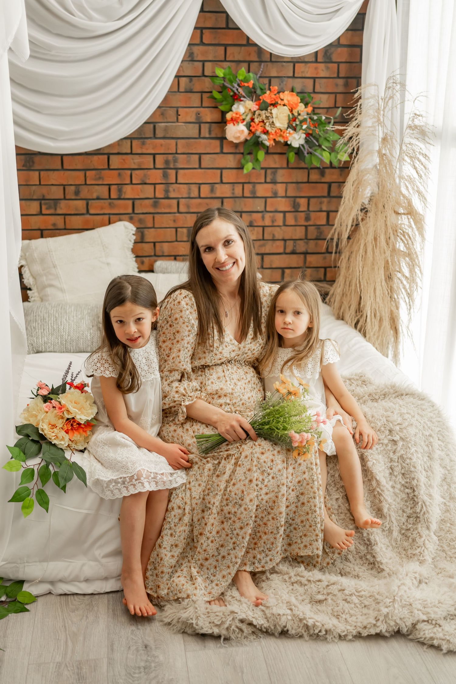 Family portrait with floral decorations and white drapes against exposed brick wall.