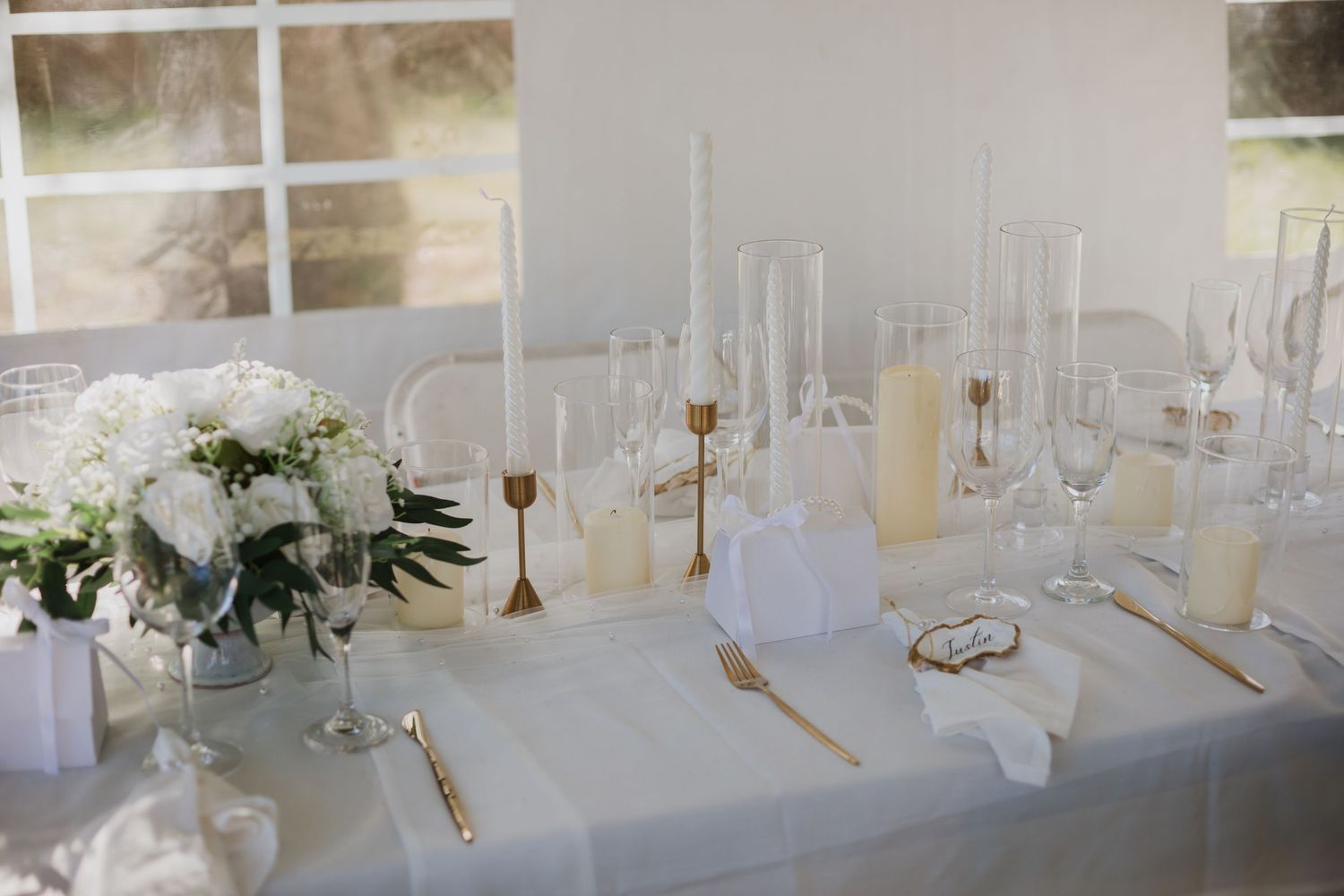 Elegant white wedding reception table setting with floral centerpiece, crystal glassware and gold candlesticks.