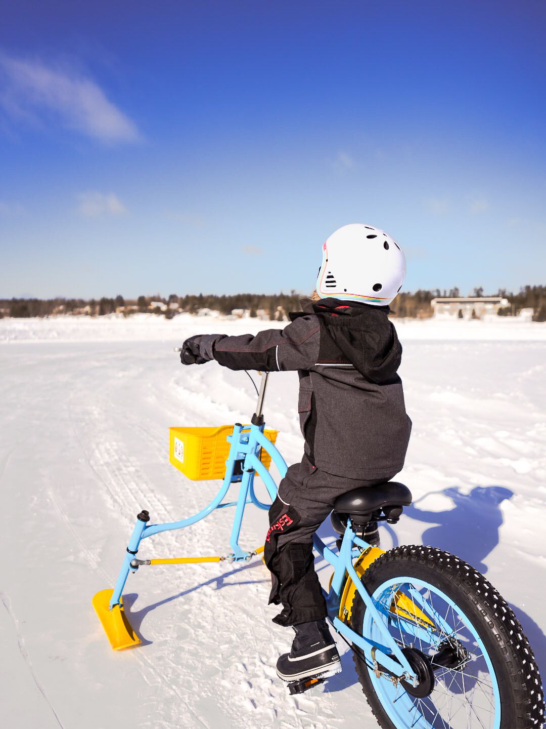 Side view of a snow bike rider traversing across a bright snowy landscape.