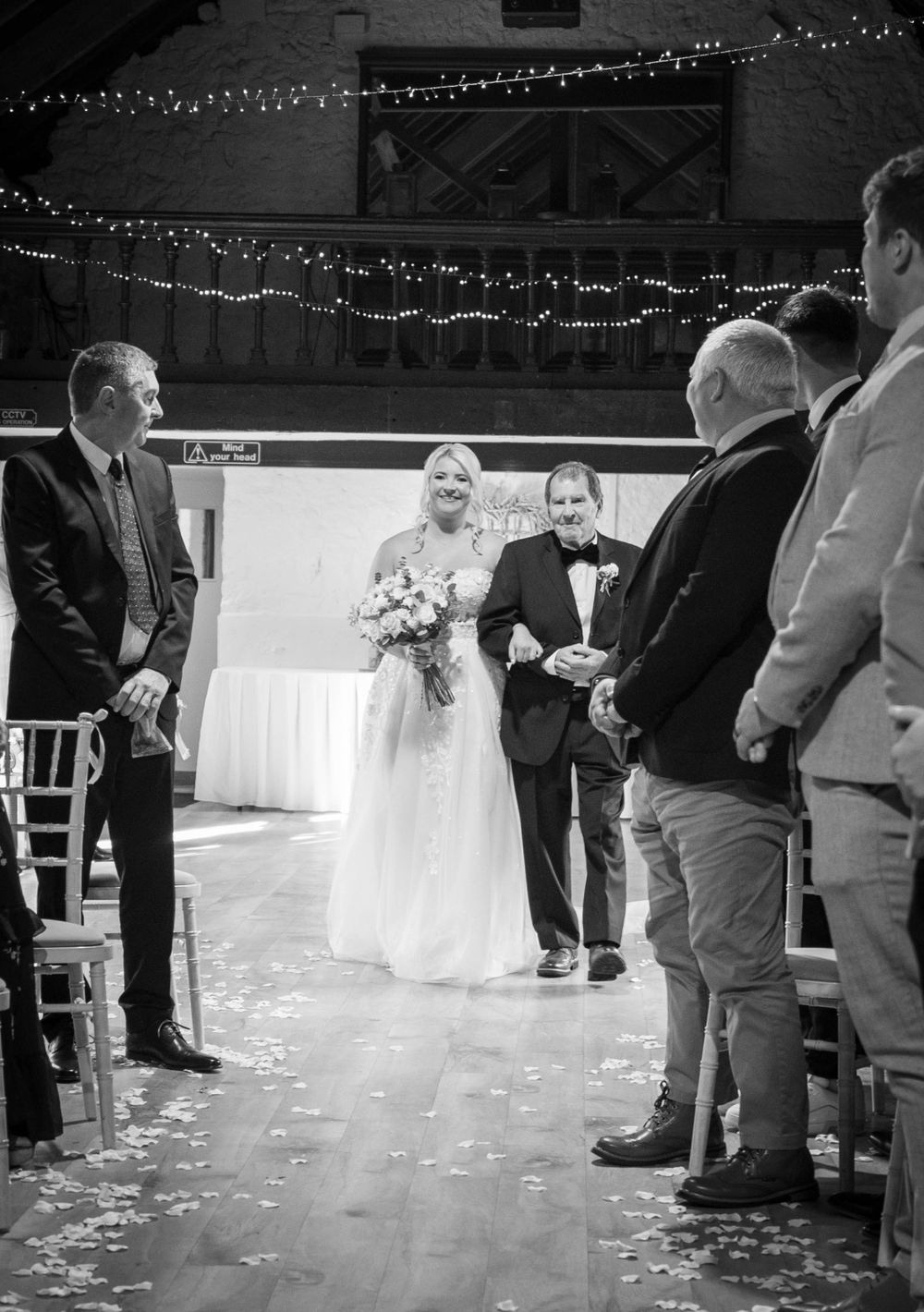A wedding ceremony in progress with guests standing and watching the couple among scattered rose petals.