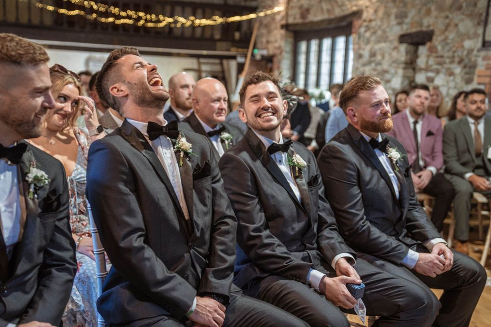 Wedding guests in formal attire laughing during the ceremony in a rustic venue.