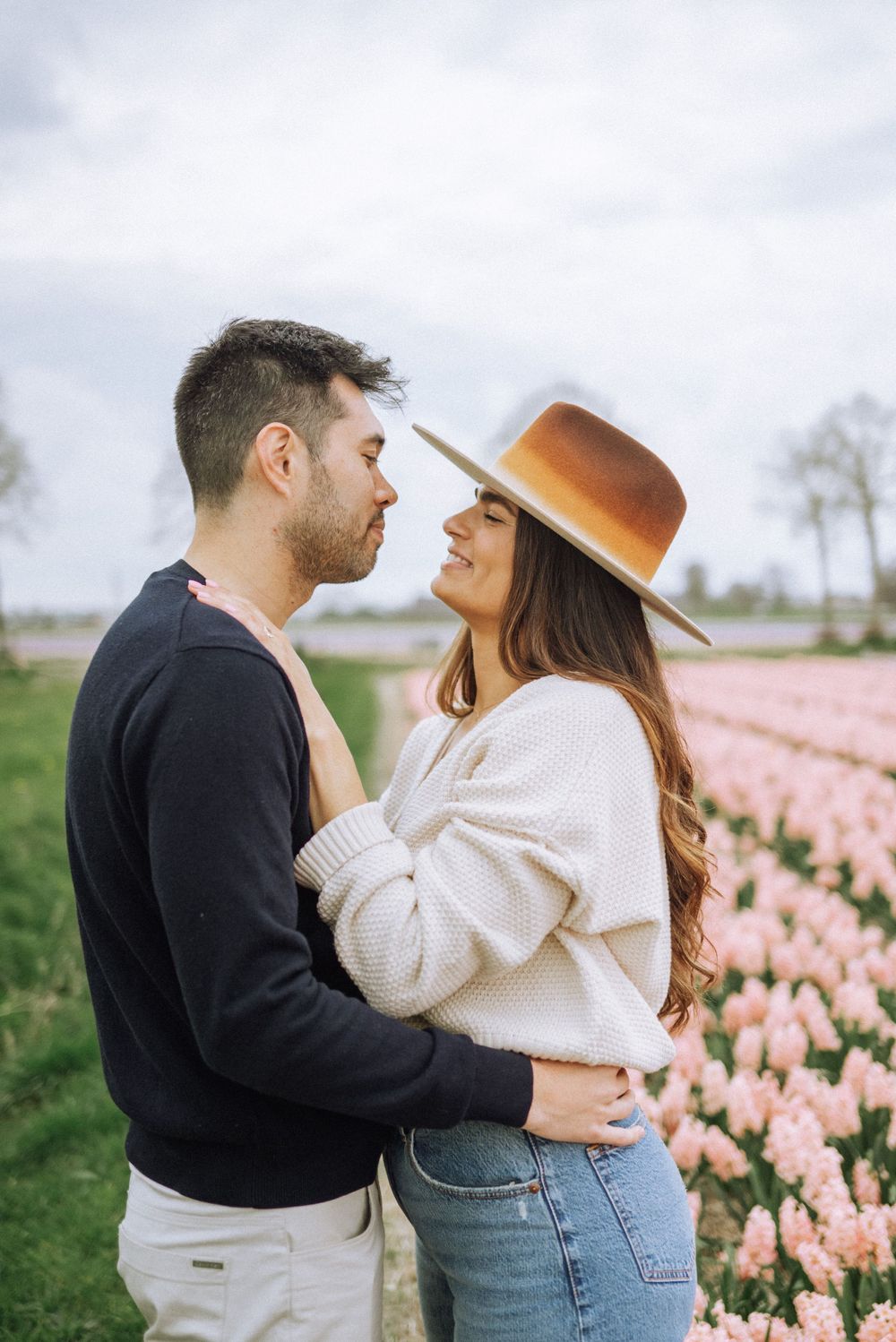 Romantic couple posing in pink tulip field wearing casual spring outfits.