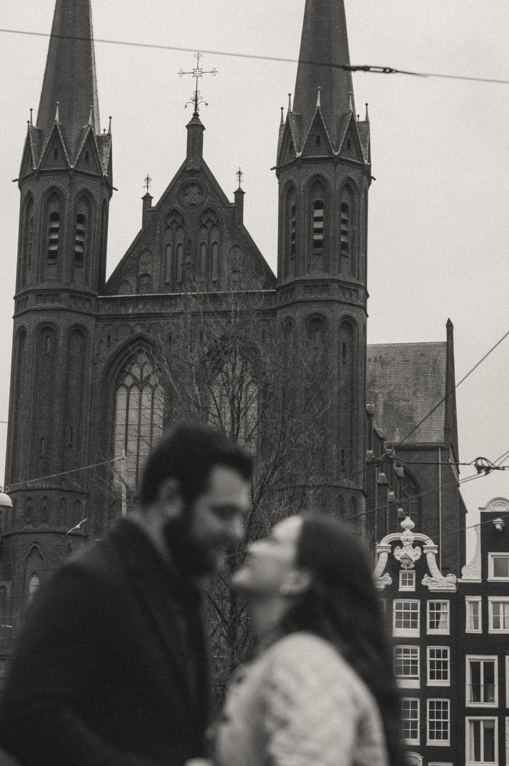 Gothic cathedral spires rise against an overcast sky in Amsterdam's historic cityscape.