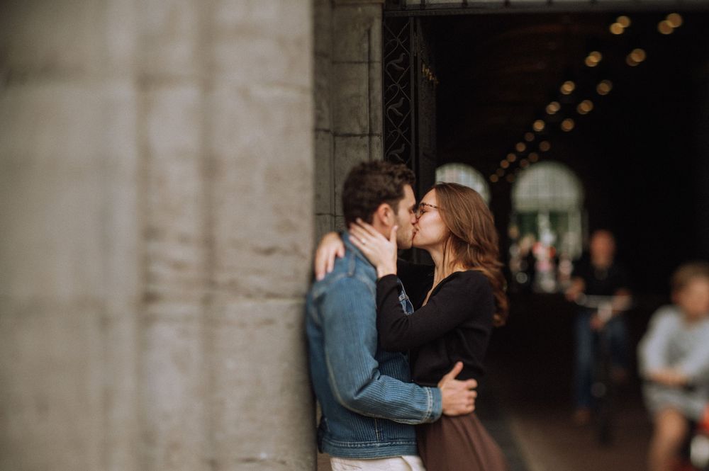 Couple sharing a romantic kiss against a stone column in an elegant archway with bokeh lights in the background. Amsterdam Rijksmuseum