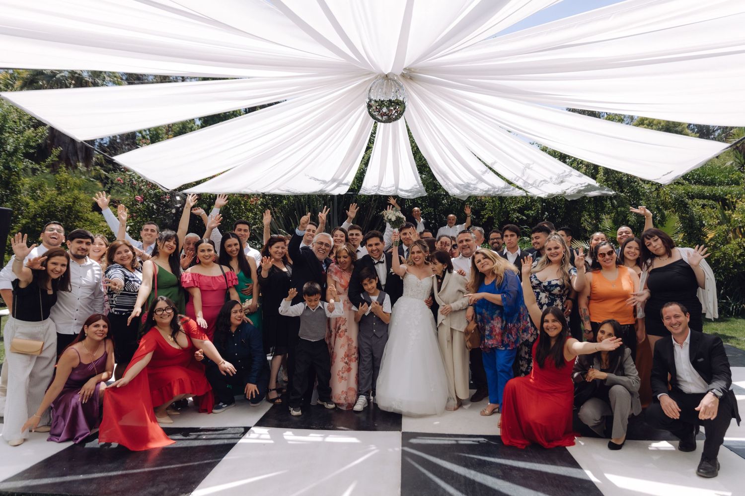 Large wedding party group photo under white draped canopy on black and white dance floor.