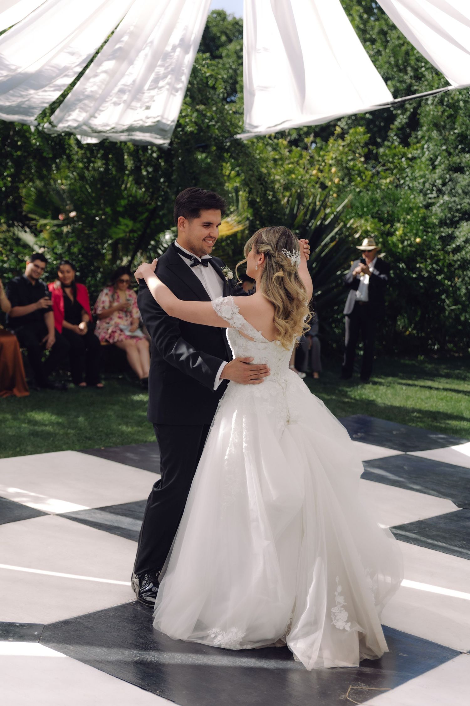 Newlyweds share an intimate first dance on black and white checkered dance floor at outdoor wedding.