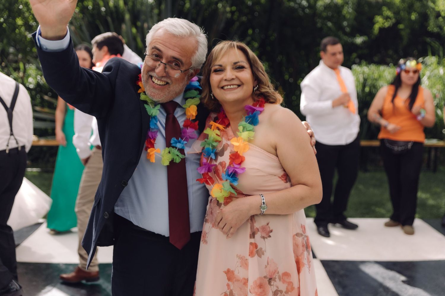 Couple posing together at outdoor wedding, man wearing colorful Hawaiian lei and waving at camera.