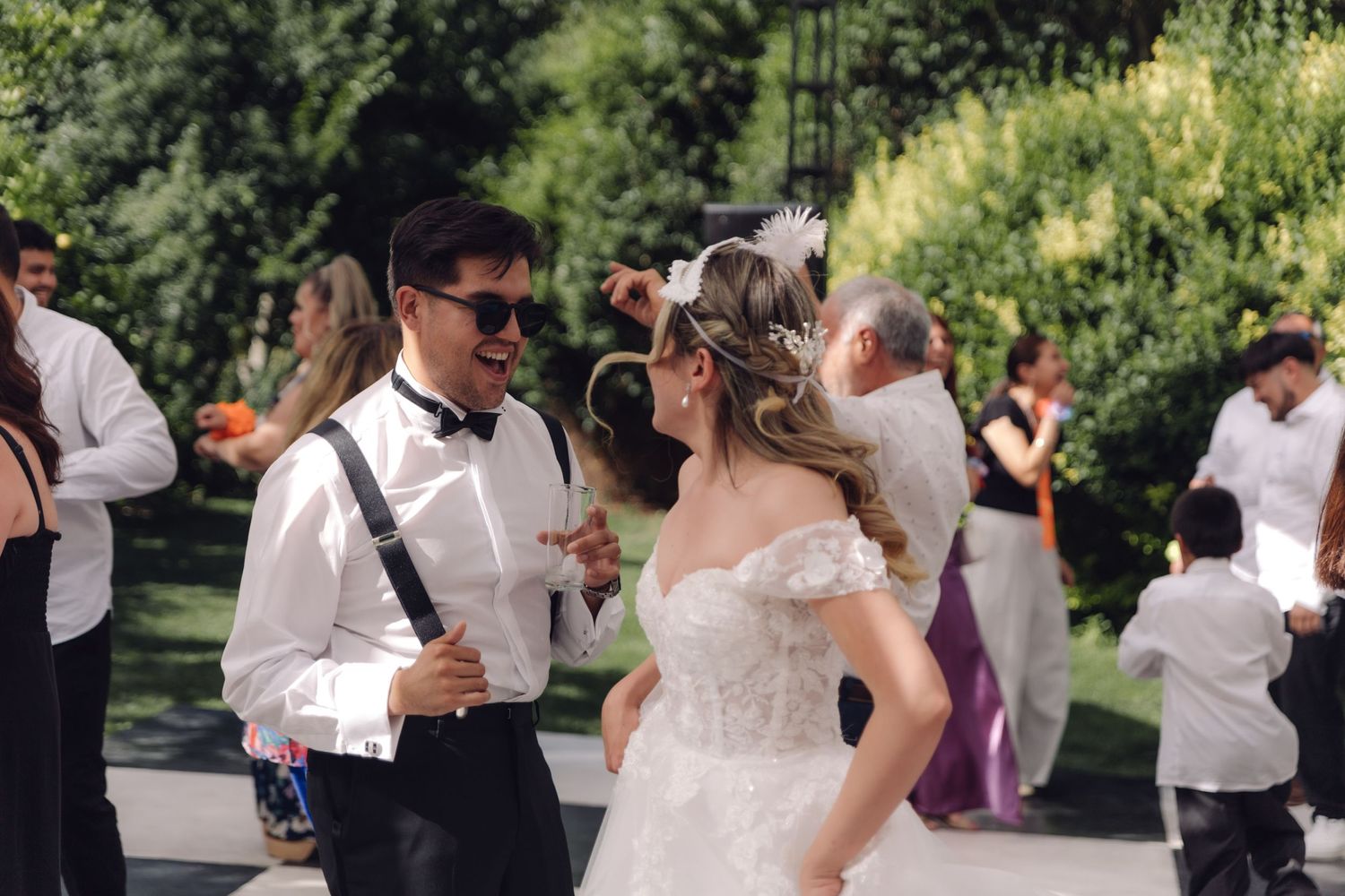 Bride in lace gown dancing with groom in white shirt and suspenders at outdoor wedding.