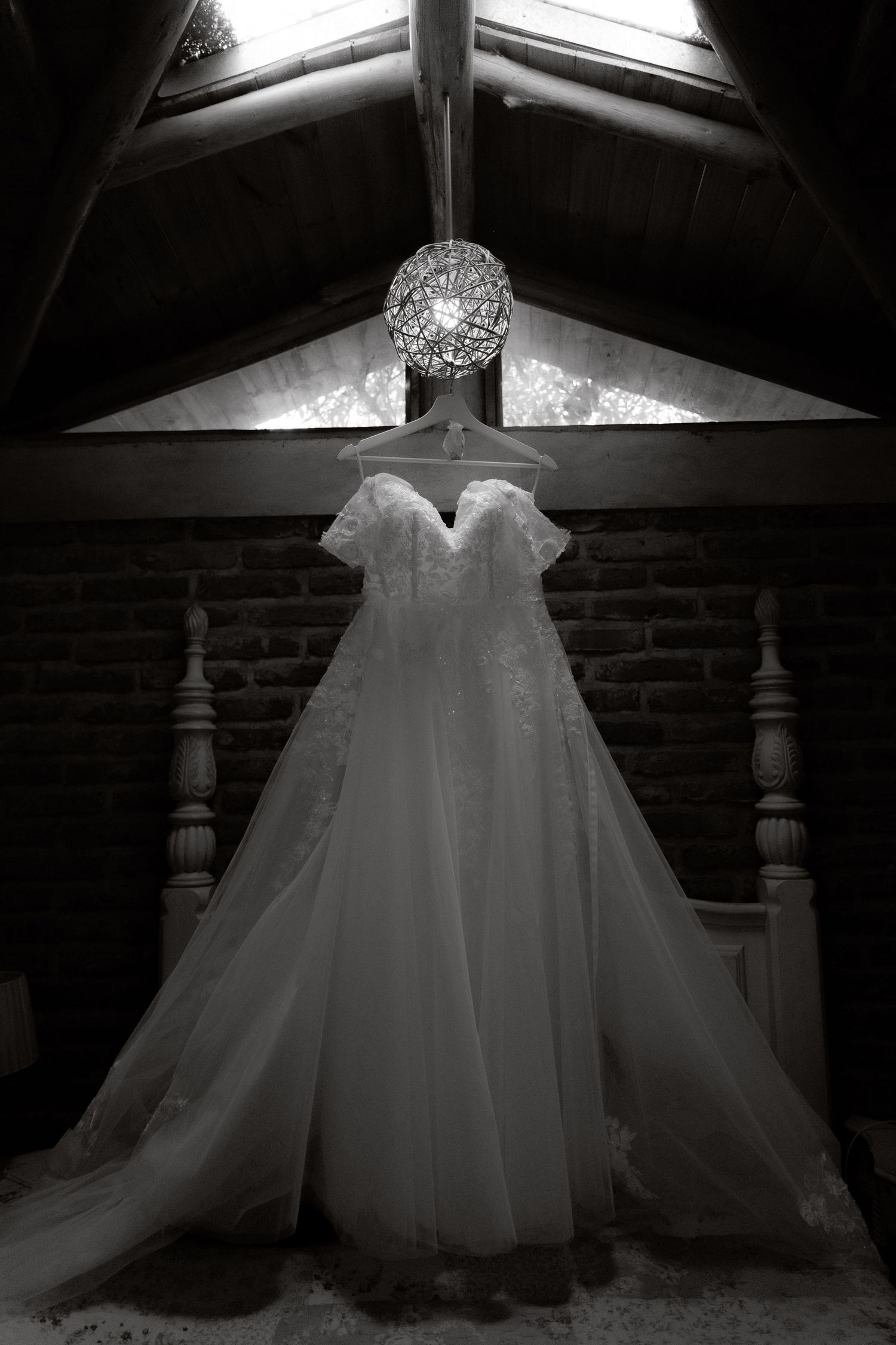 Black and white photo of an elegant wedding dress hanging under a crystal chandelier.