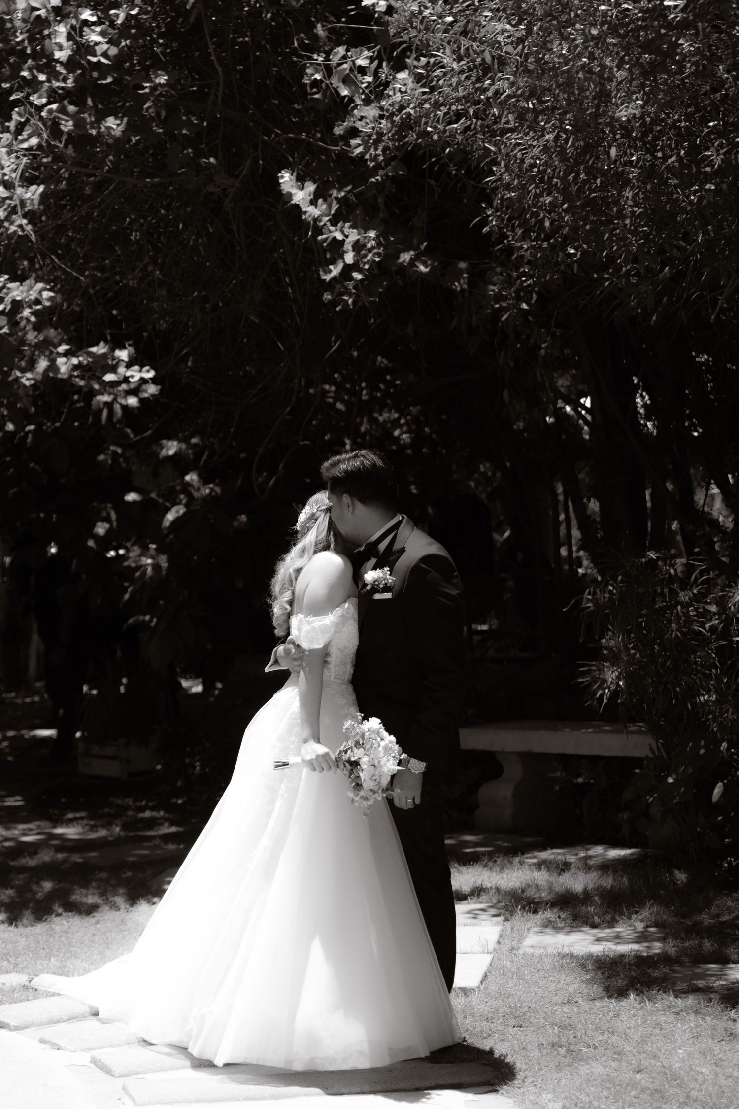Black and white photo of bride and groom sharing intimate kiss in garden on wedding day.