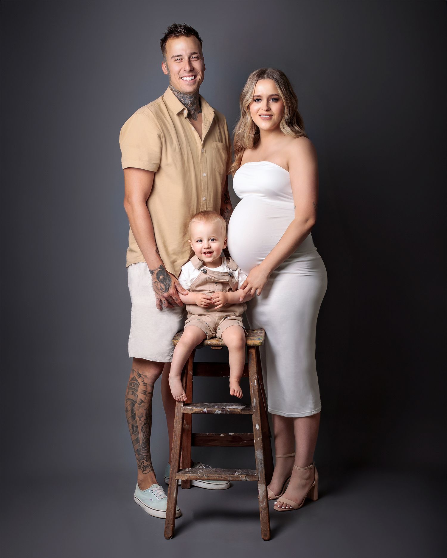 Mother, father and child looking directly at the camera, beautiful and engaged family portrait. Against a gray paper backdrop.