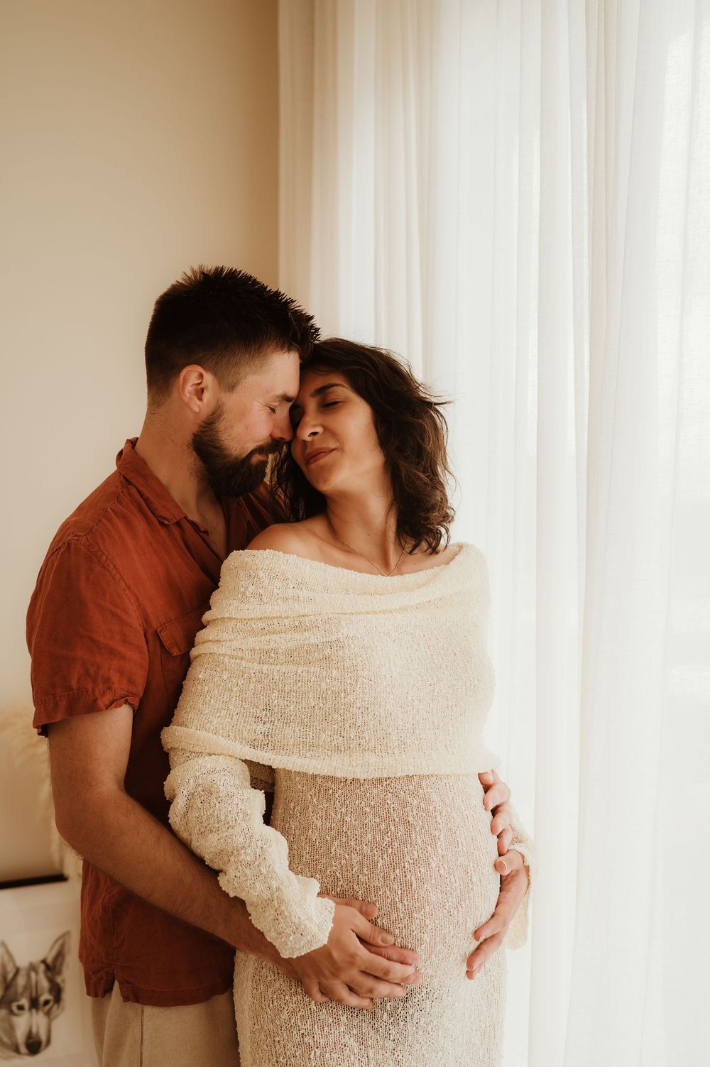 Couple shares intimate moments in a bright room, with sheer white curtains and cozy knit blanket.