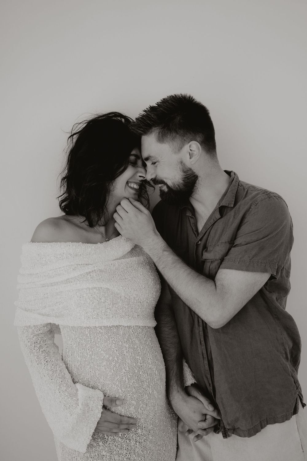 Black and white photos capture tender moments between a couple wrapped in a soft white blanket.