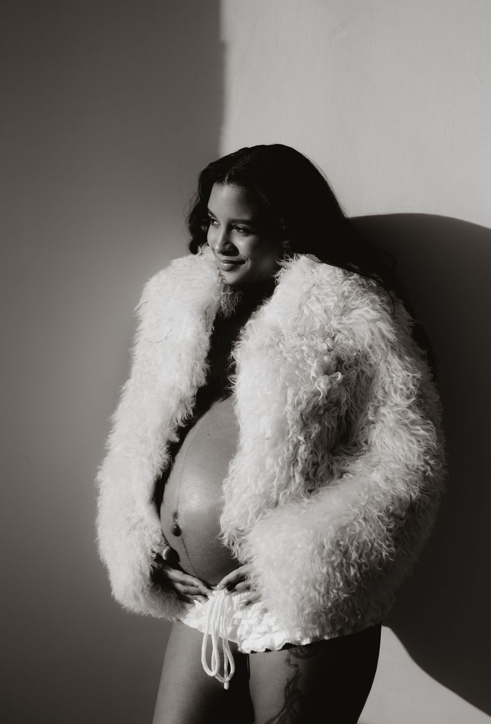 Artistic black and white portrait featuring a fluffy white fur wrap against a plain background.