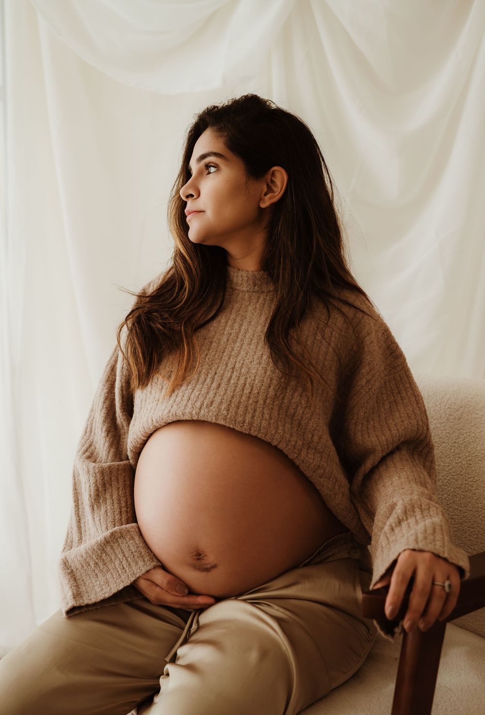 A series of artistic maternity photos showing a pregnant woman in a cozy beige sweater against a white backdrop.