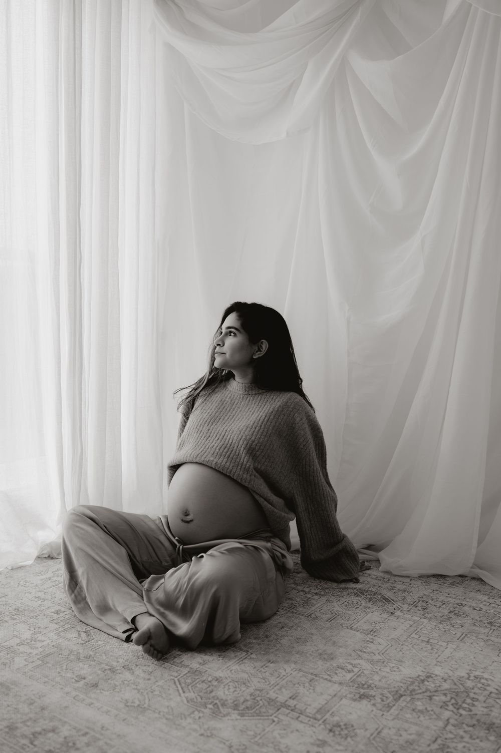 A series of black and white photographs showing a figure in a sweater reclining against a white backdrop.