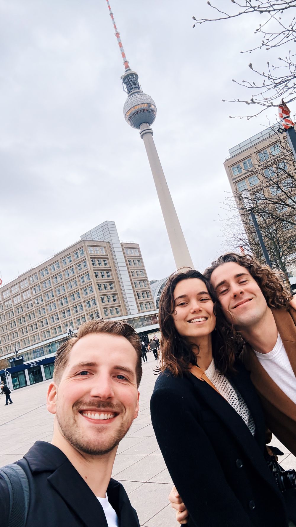 The Berlin TV Tower (Fernsehturm) dominates the skyline as visitors take a photo in Alexanderplatz.