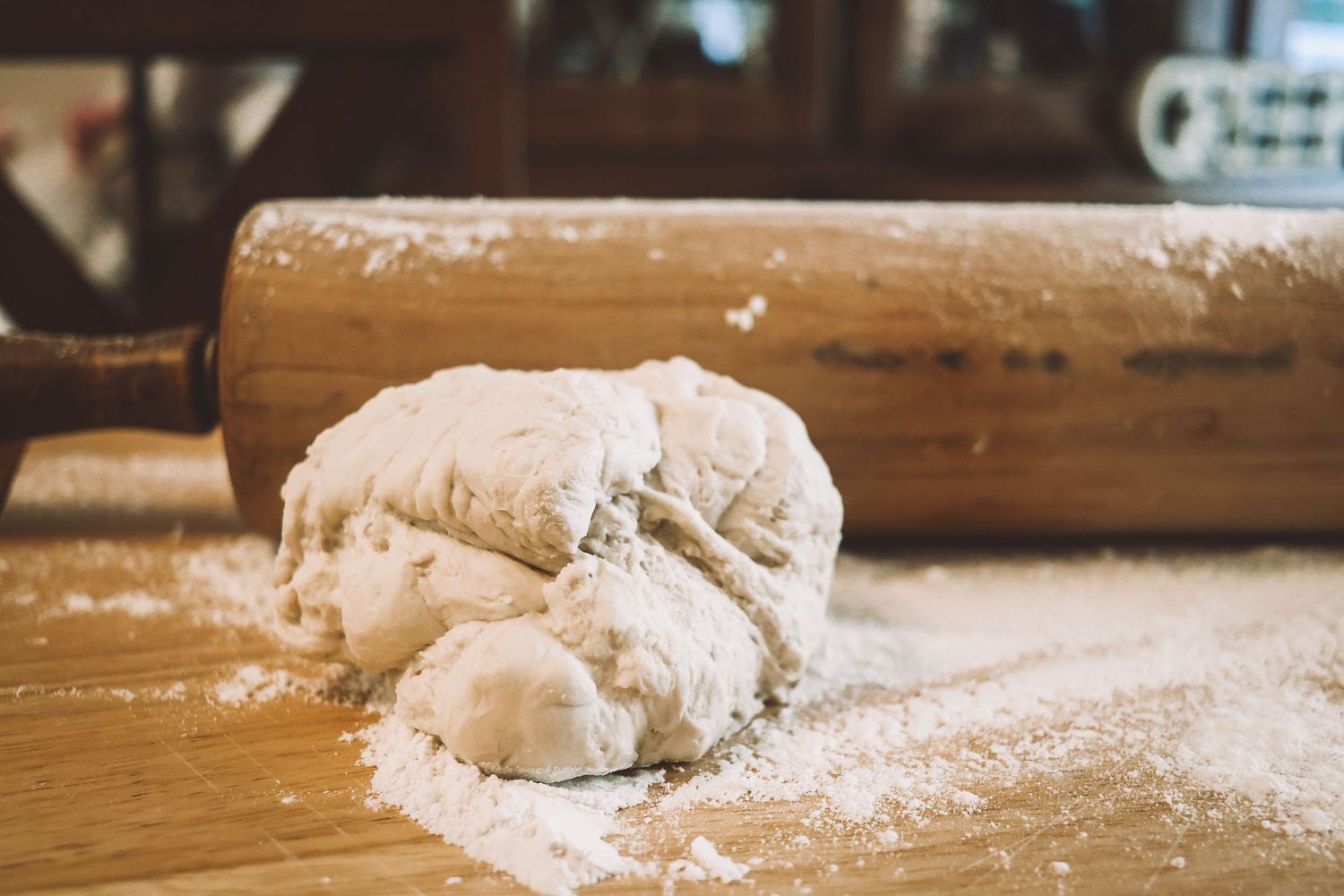 Raw bread dough on a wooden cutting board with flour and rolling pin in rustic baking scene.