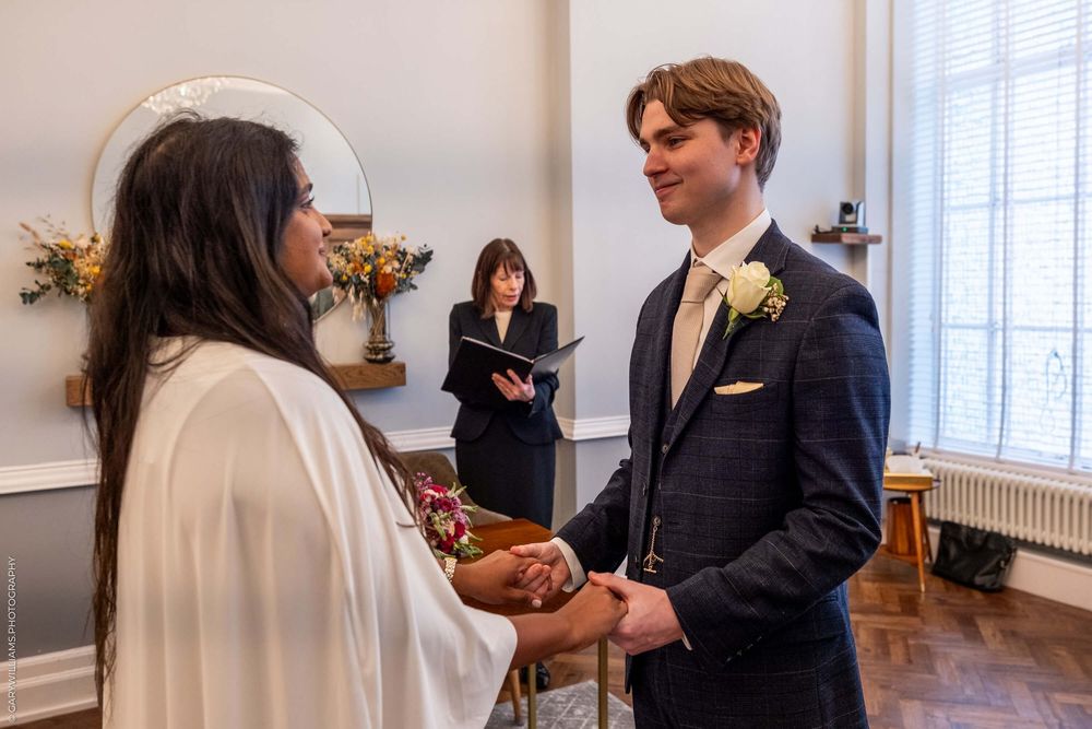 A couple exchanges vows during an intimate indoor wedding ceremony with an officiant standing behind them.