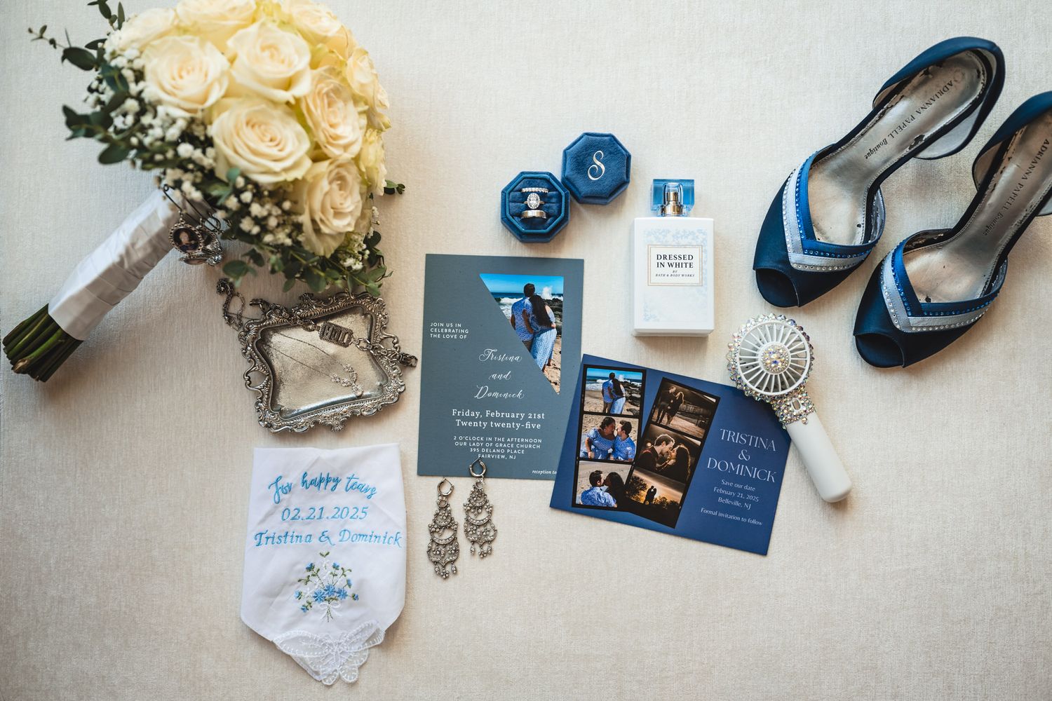 Wedding details flatlay with blue and white stationery, rings, and white roses.