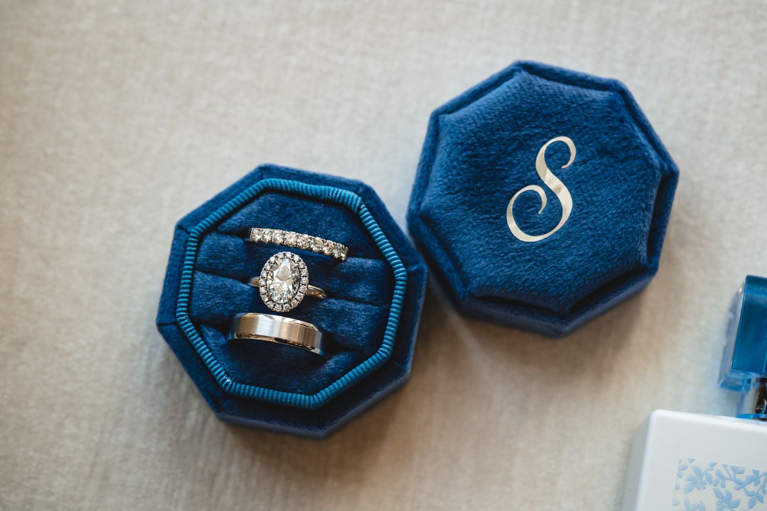 Engagement ring and wedding bands displayed in navy blue velvet ring boxes.