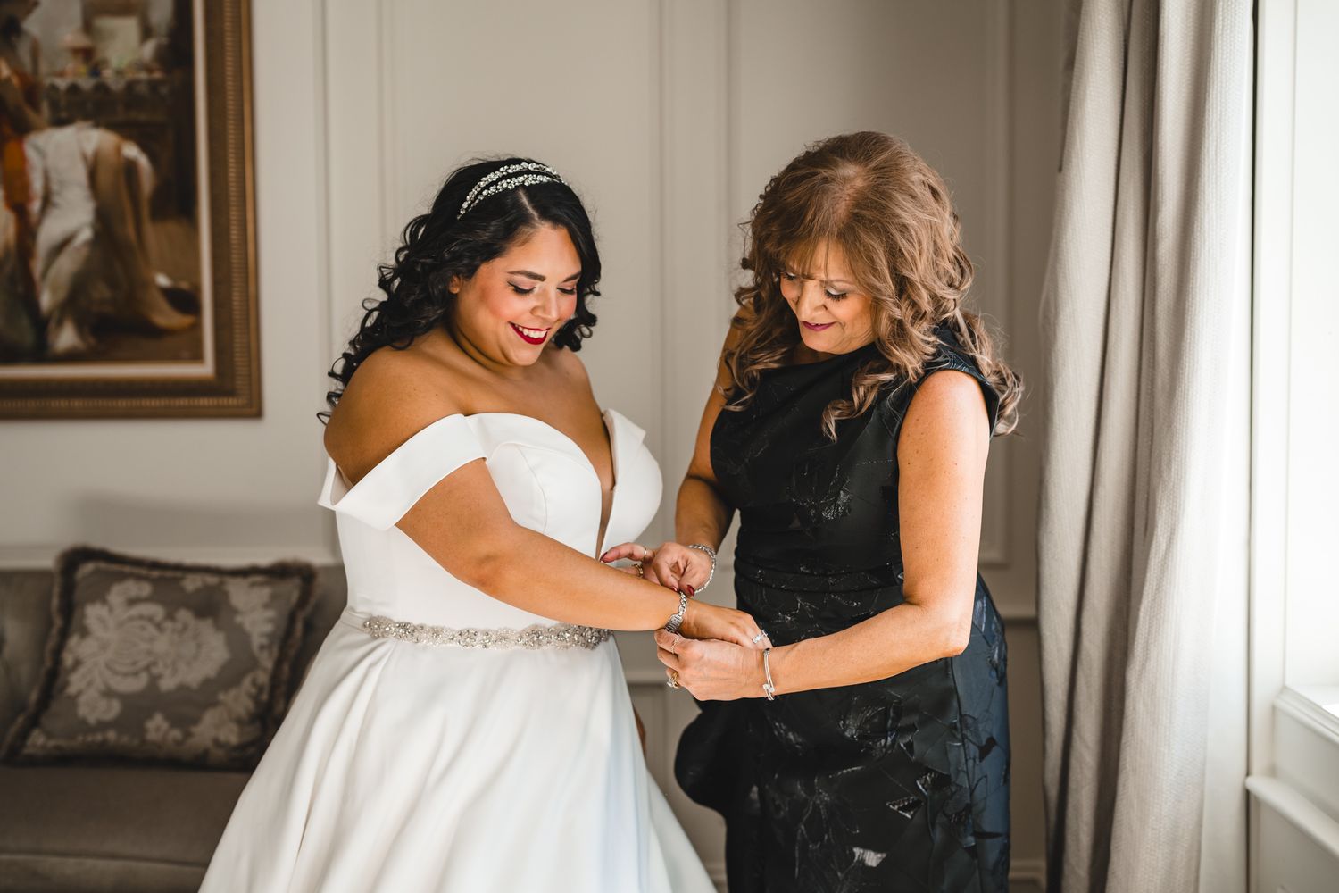 A bride getting ready with assistance as someone helps adjust her wedding dress and shoes.