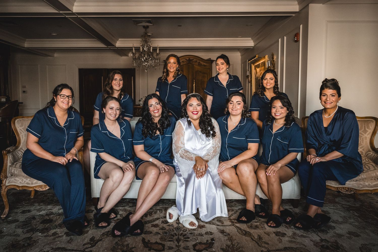 Wedding party in navy blue attire sits together on floor for casual group photo.