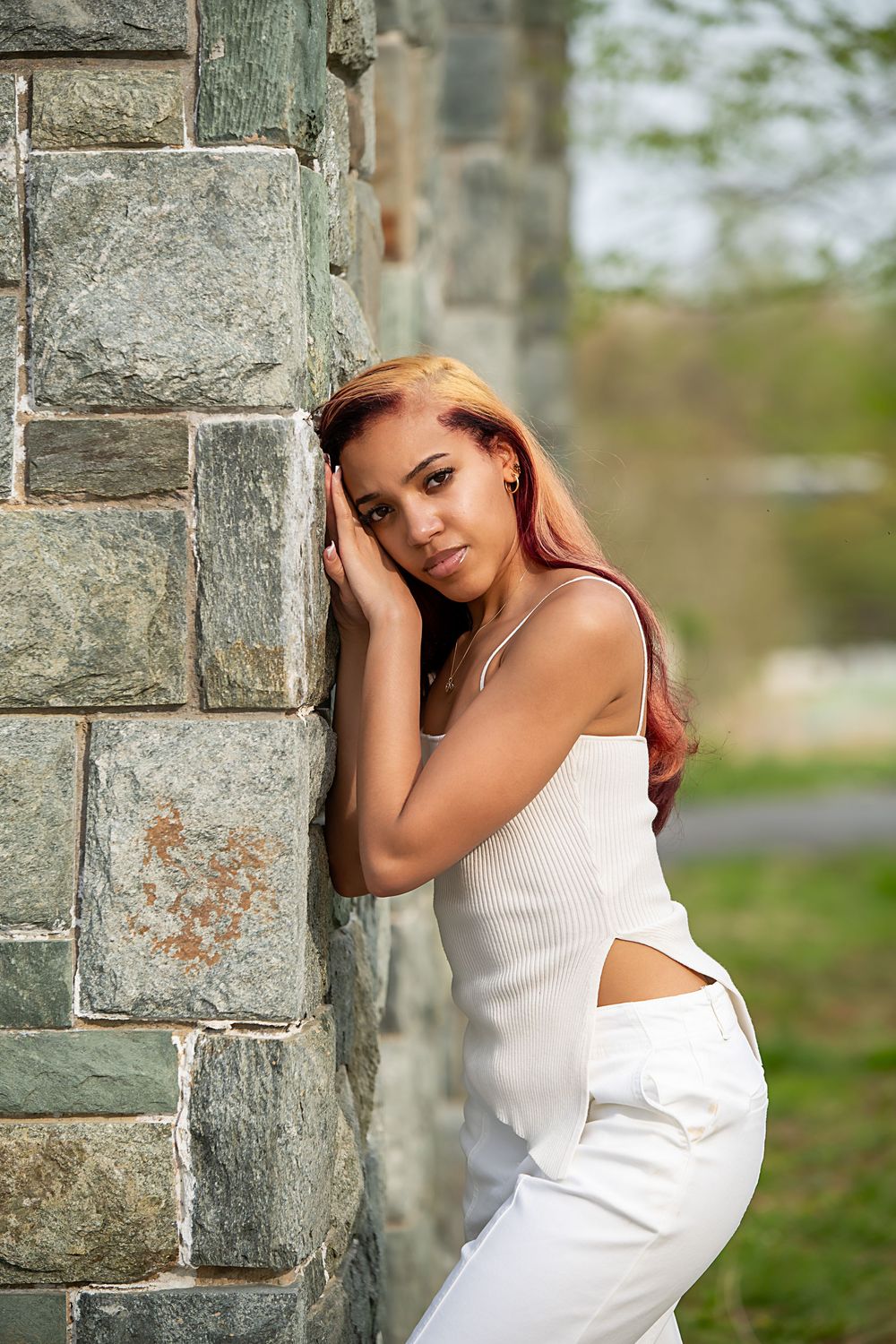 Fashion portraits against stone wall featuring white dress and natural lighting.