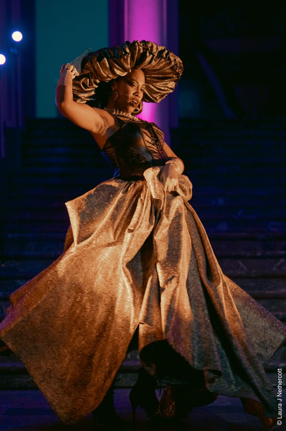 Performer in gold dress twirling on stage under theatrical lighting.