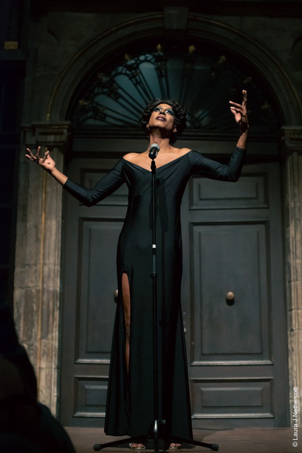 Dramatic performance of singer in black gown against ornate doorway backdrop.