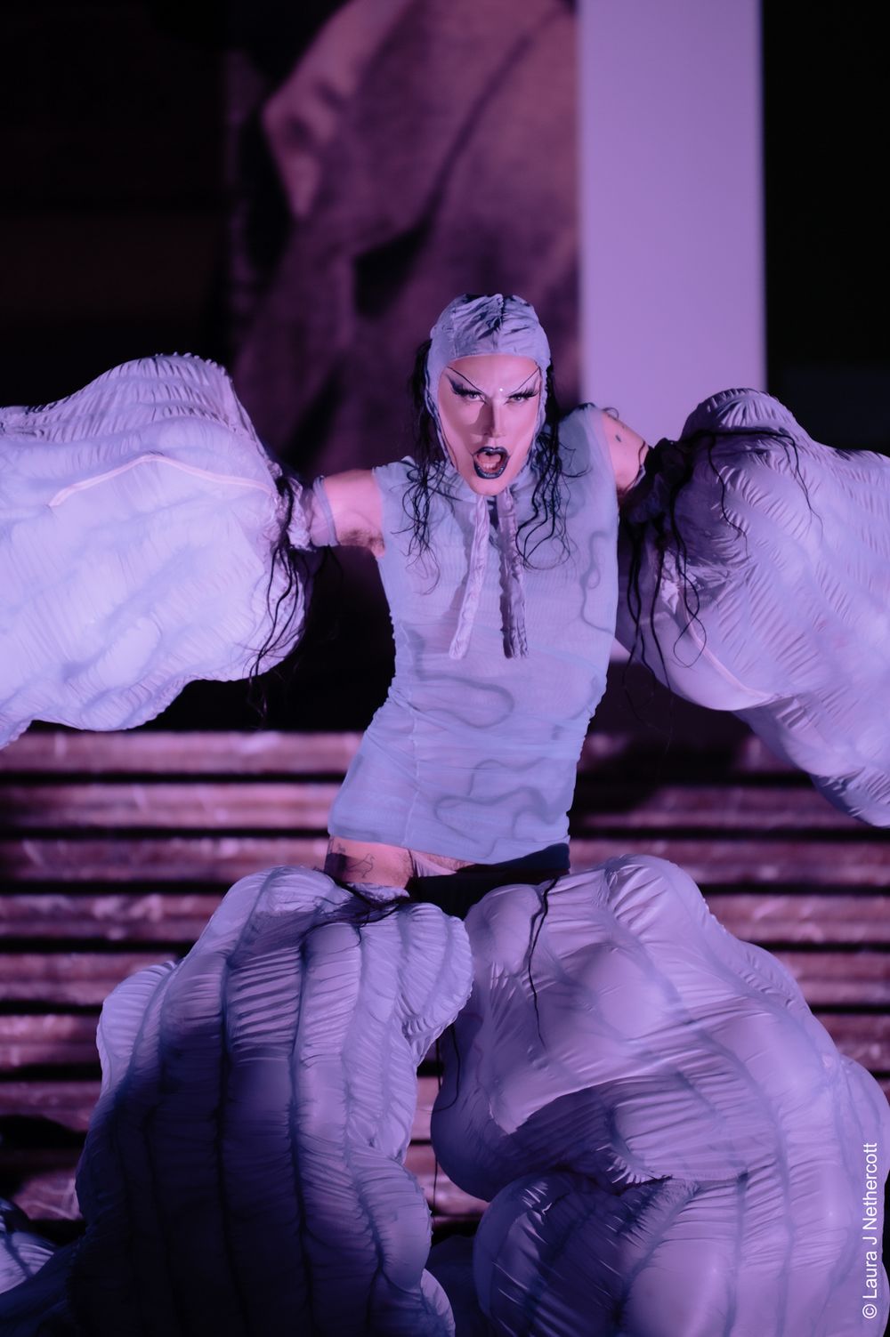 Dramatic dance performance in white costume under purple lighting creating striking movement sequence.