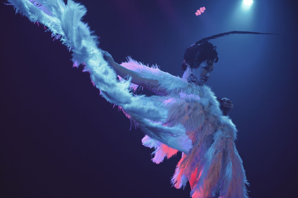 Performer in flowing white costume with blue lighting effects during theatrical dance performance.