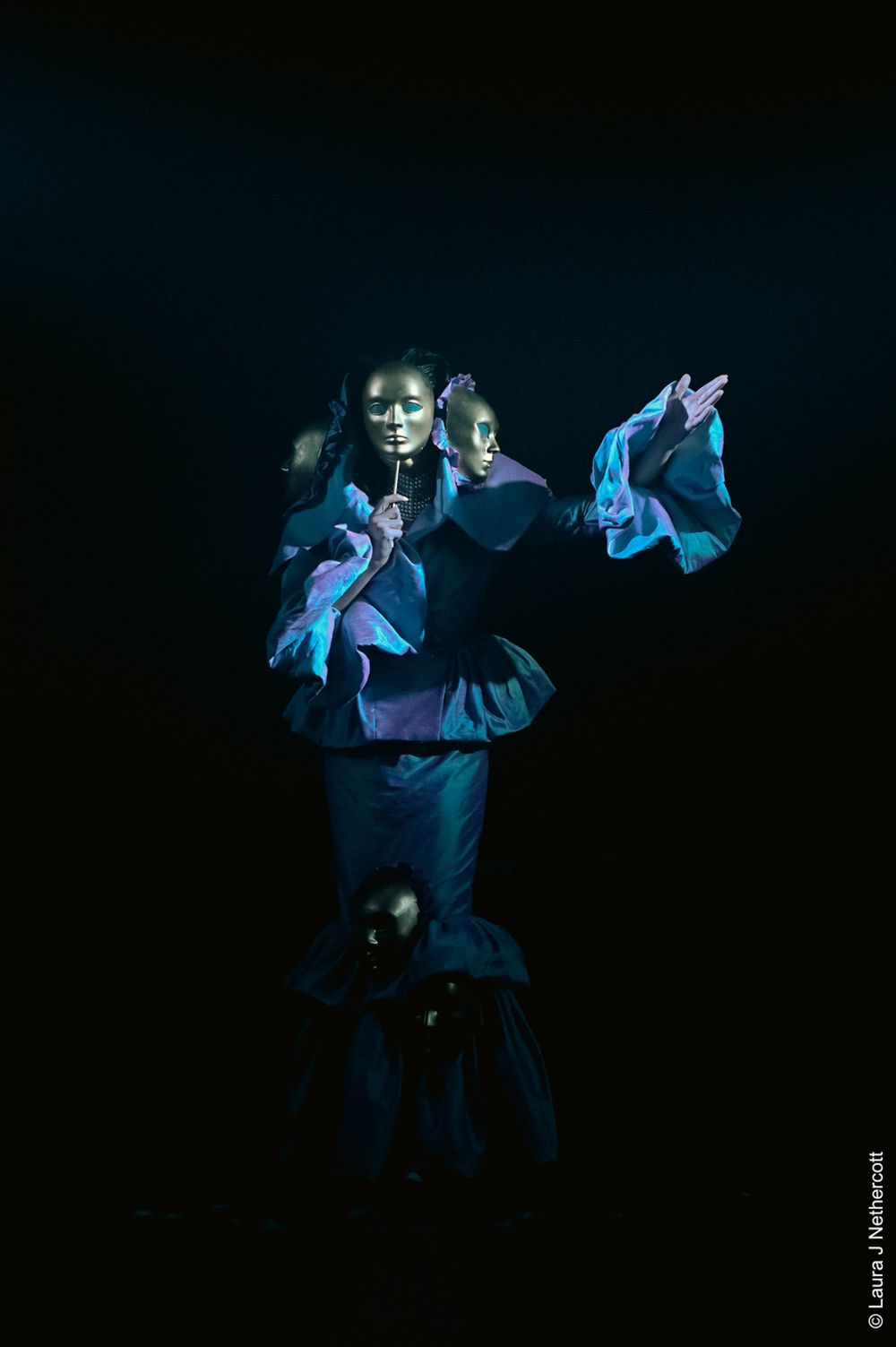 Dancers performing in dramatic blue stage lighting with flowing movements.