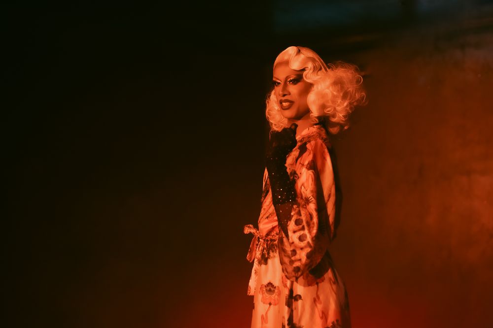 Orange-tinted theatrical scene with dramatic lighting and shadowy figures.