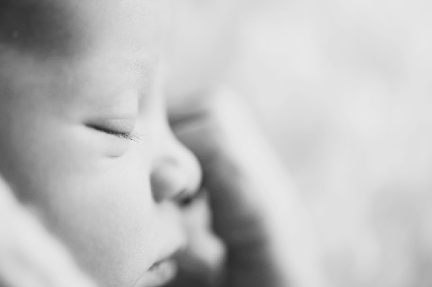 A close-up black and white photograph shows a peaceful sleeping baby's face in soft focus.