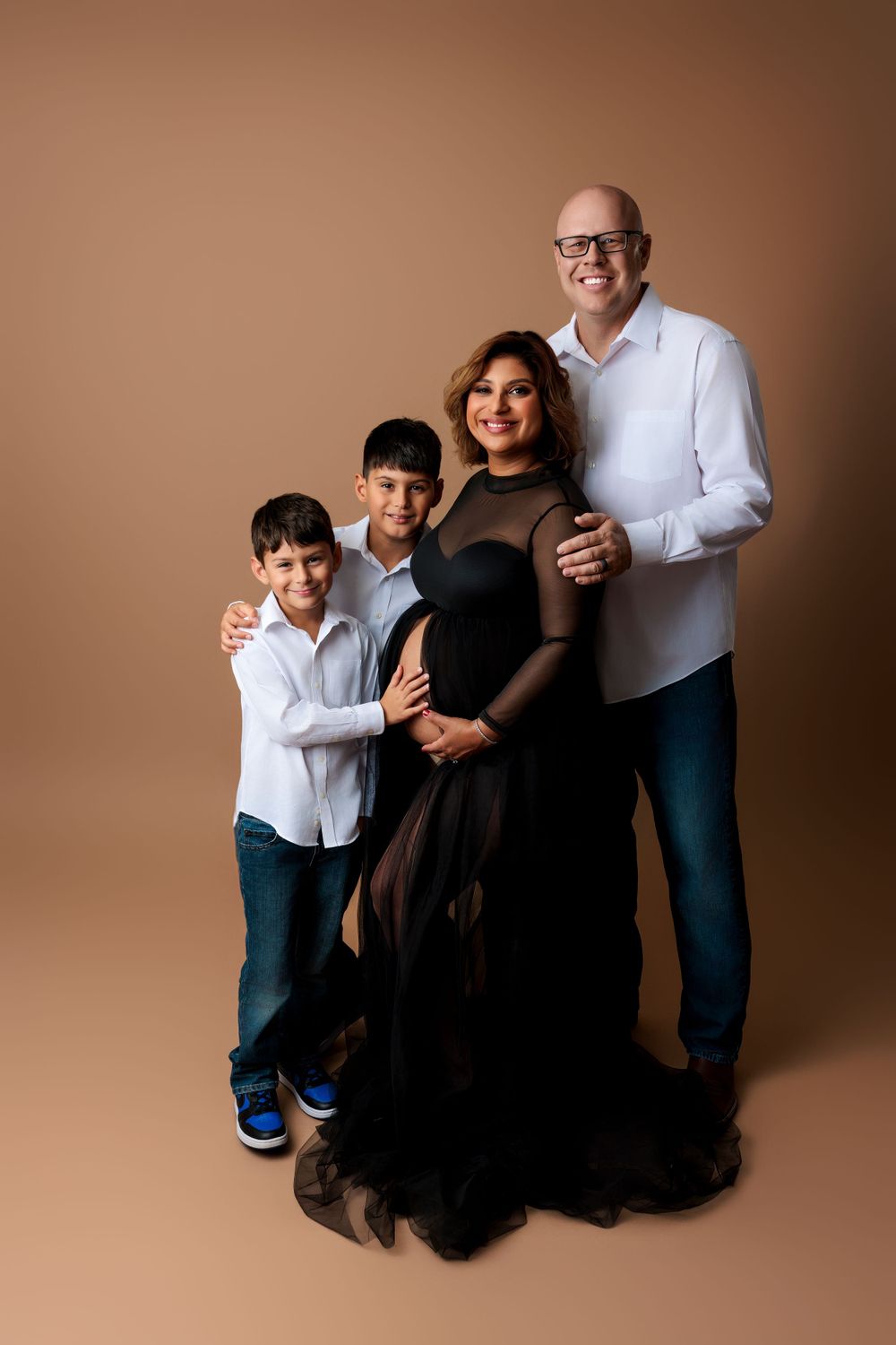 A family portrait against a brown backdrop with two children and their parents dressed in coordinating outfits.