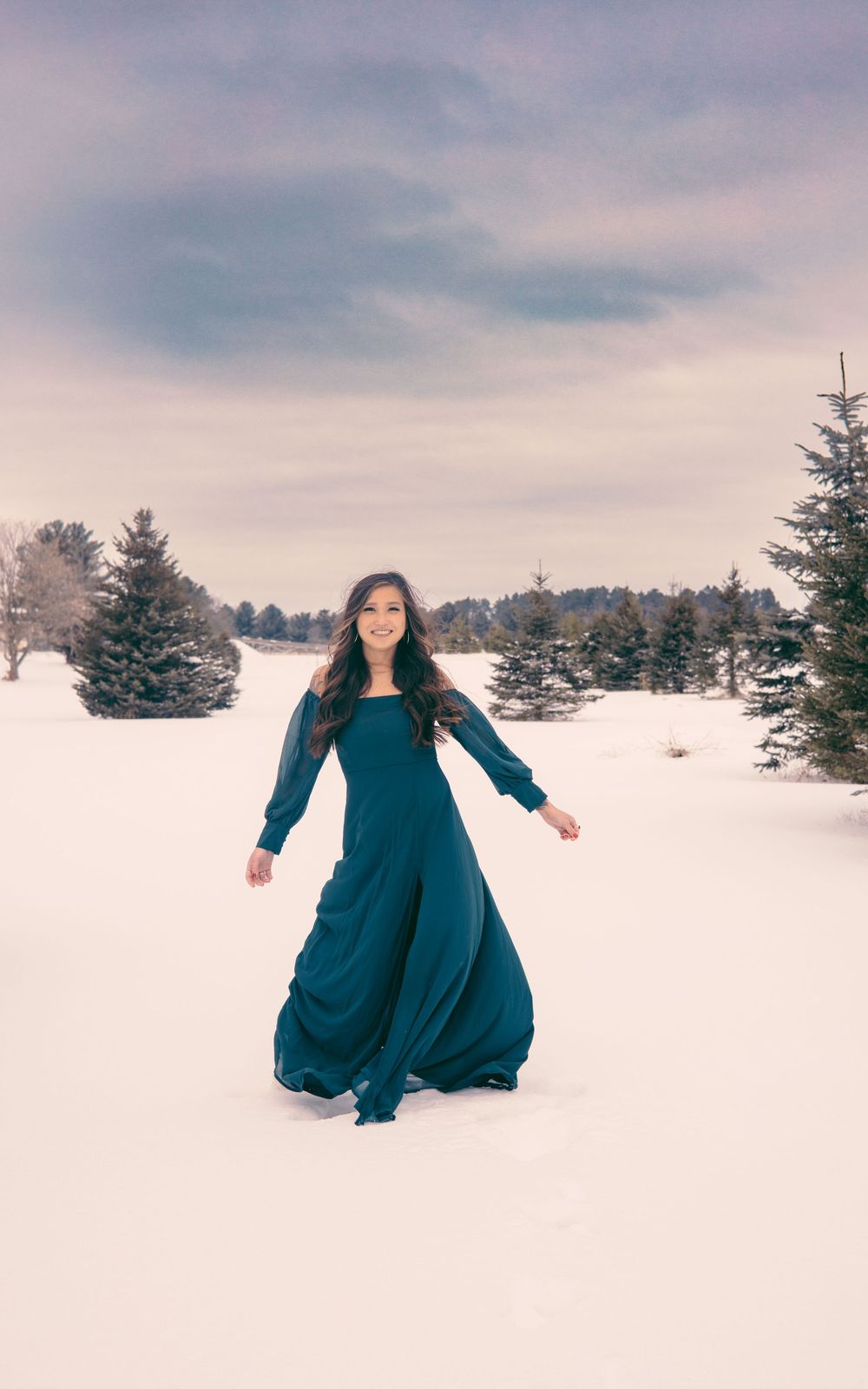 Person in flowing teal dress twirling in snowy winter landscape.