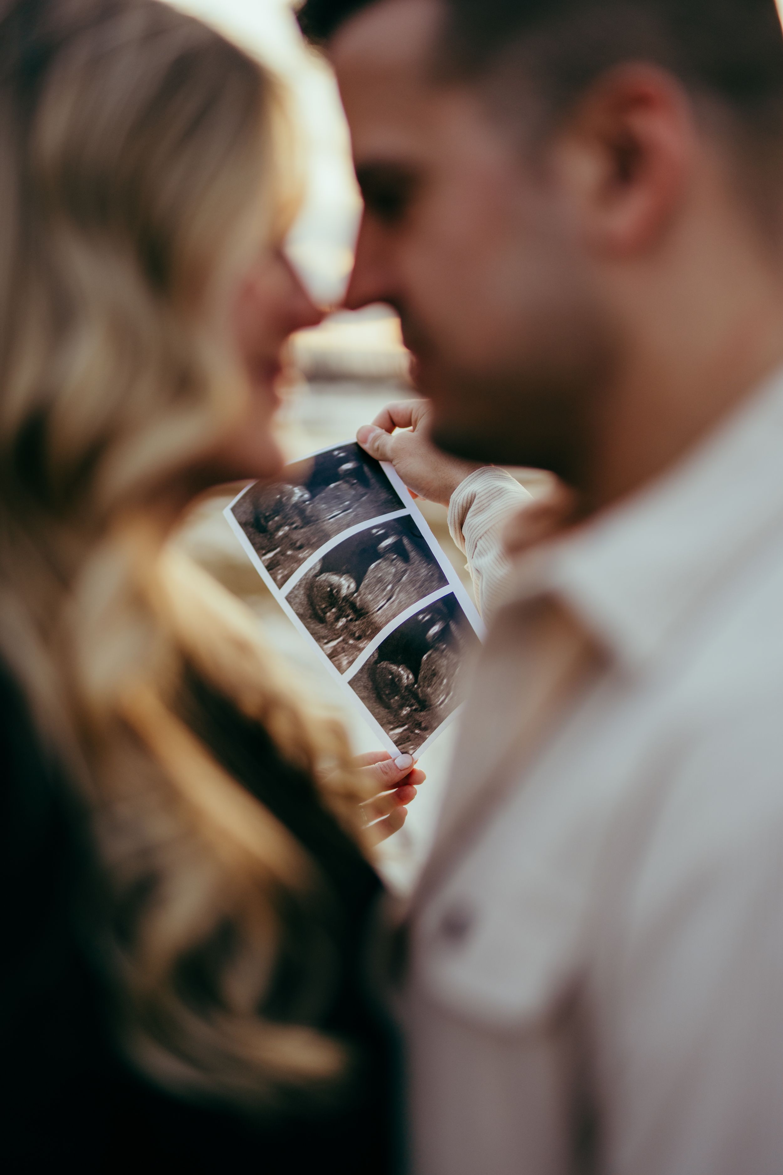 Close-up of a couple holding an ultrasound photo while sharing an intimate moment together. Fort McMurray Alberta Photographer