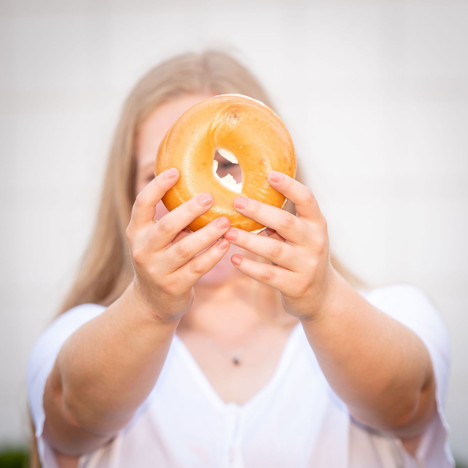 Person holding up a giant bagel in front of their face against a light background.