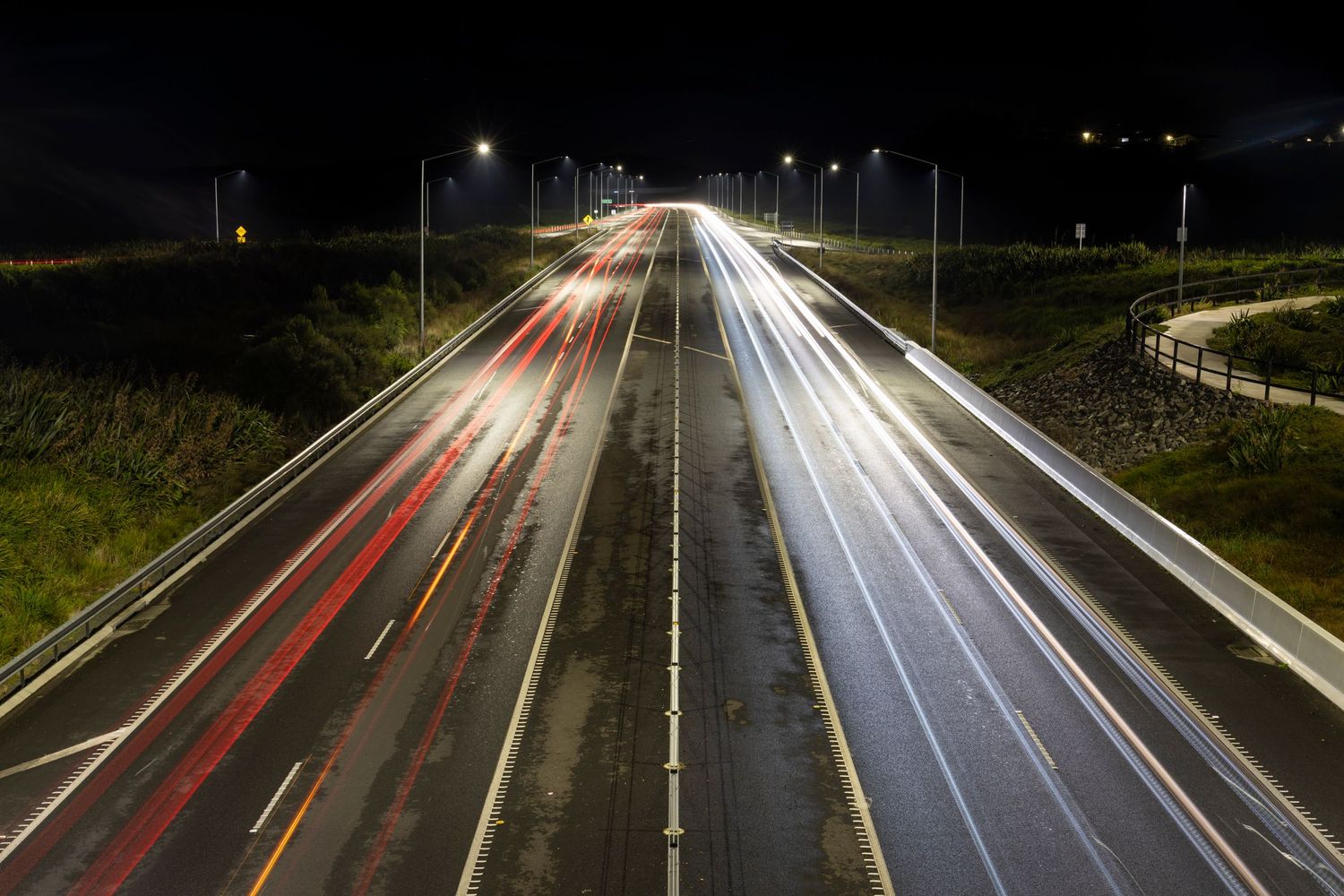 Long-exposure view of car headlights and taillights streaking along a multi-lane highway under streetlights at night.