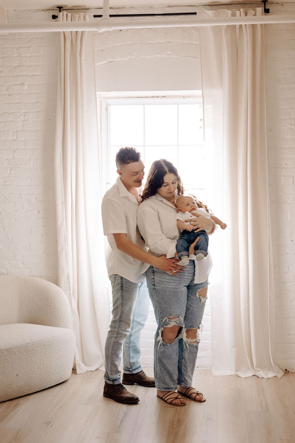 Newborn photographer in Havelock NC capturing parents holding their newborn by a bright window during a natural lifestyle session.