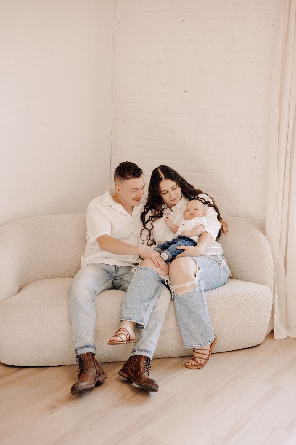 Lifestyle newborn photography in Havelock NC — parents cuddling their baby on a neutral couch during an in-home family session.