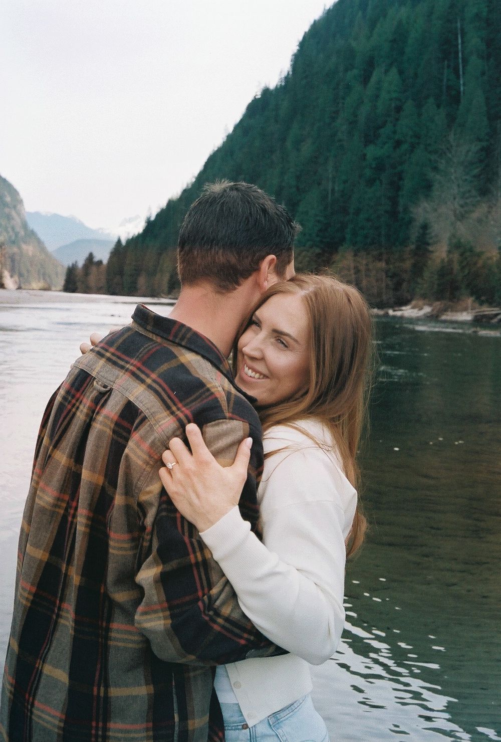 A romantic embrace captured against a backdrop of mountains and calm waters.