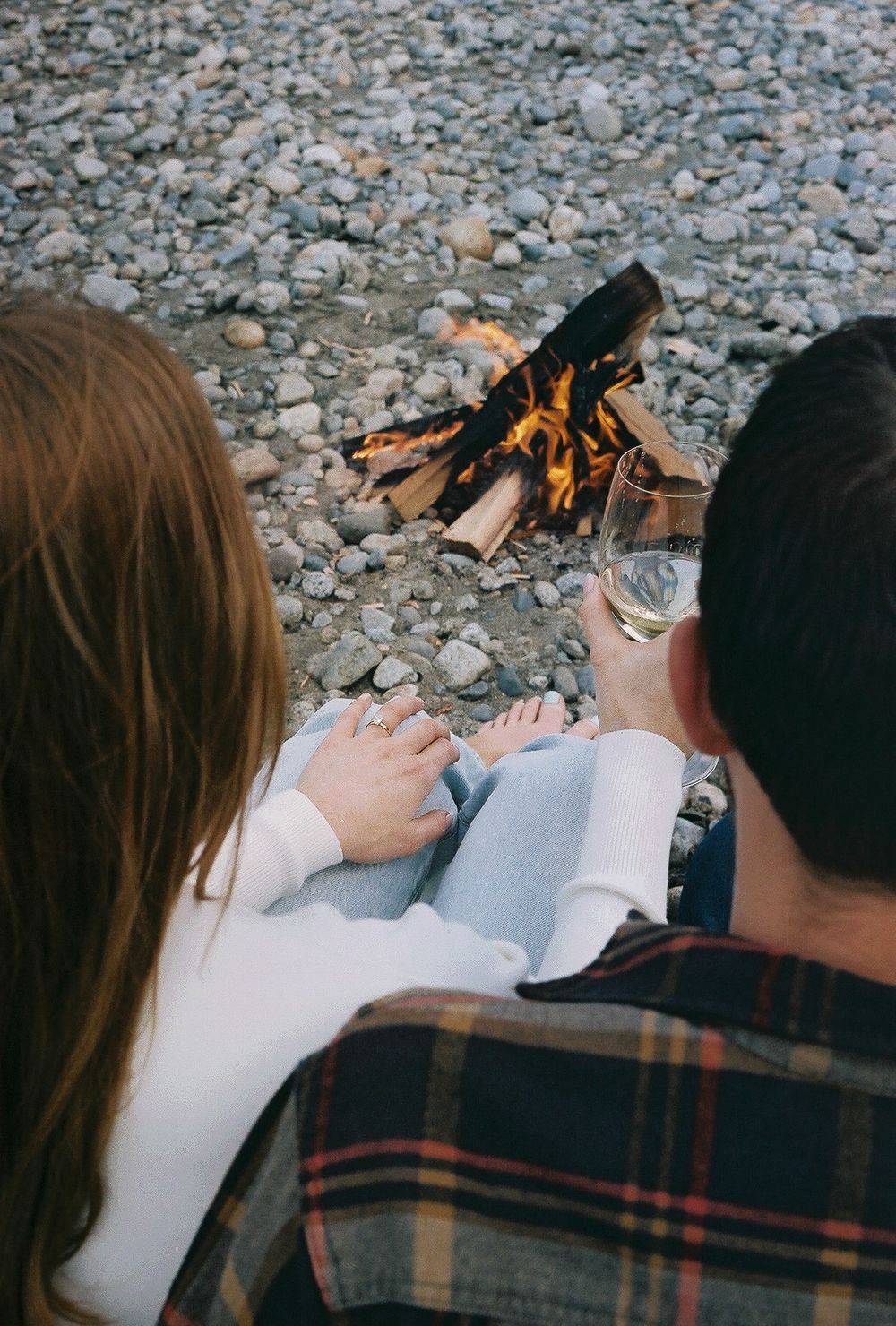 Cozy scene of reading together by campfire on rocky beach.