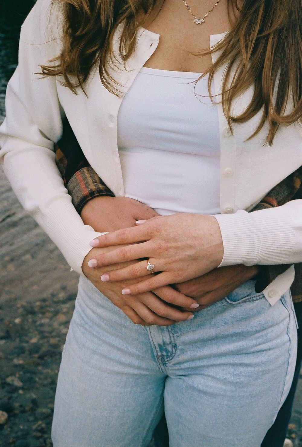 Close up of hands wearing white sweater and light blue jeans.