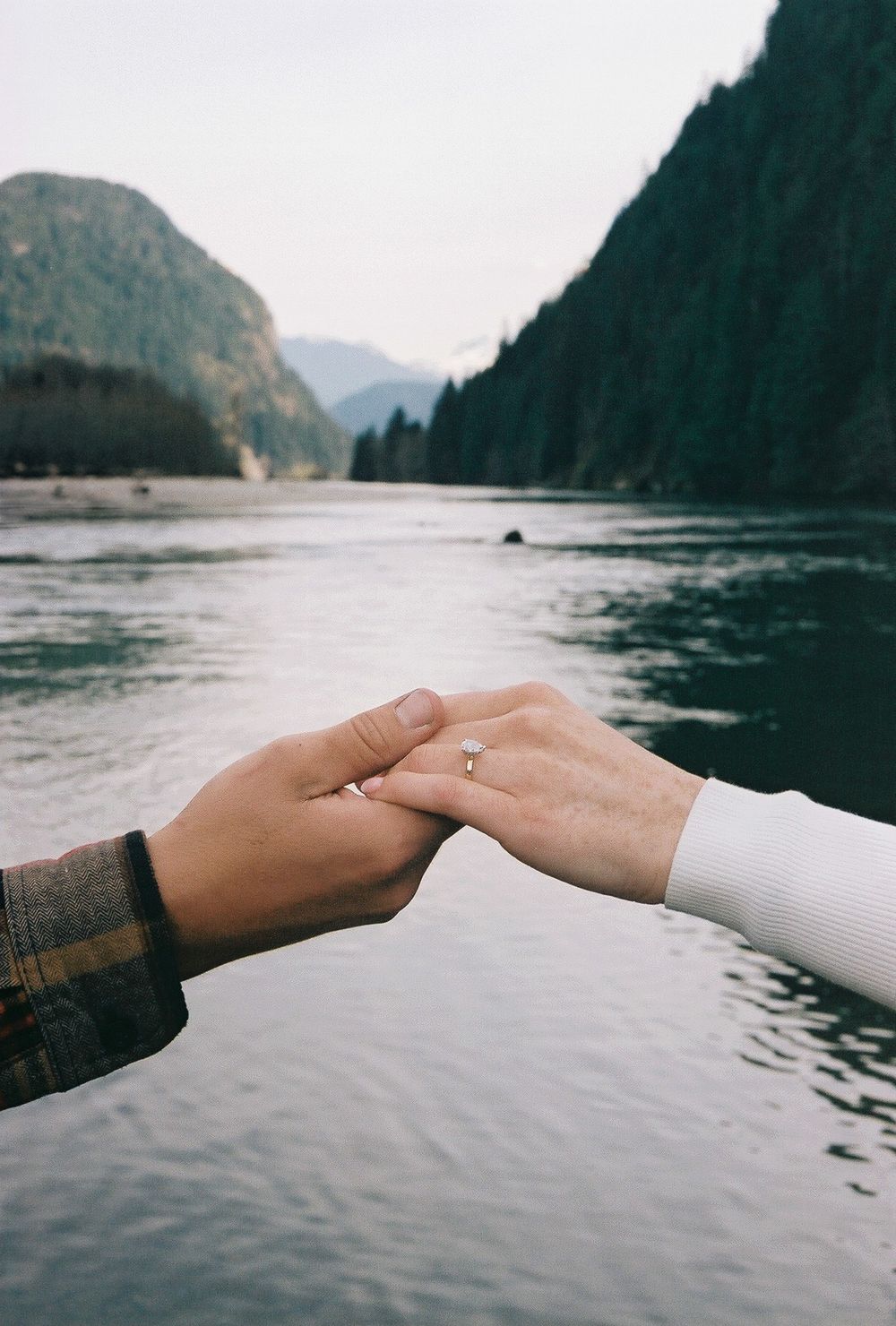 Two hands reaching towards each other against mountain lake backdrop.